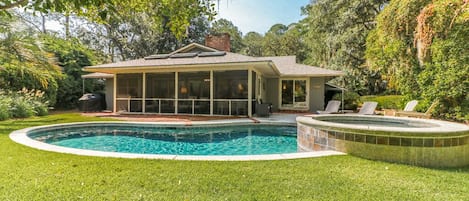 Una casa con piscina, rodeada de césped cuidado y árboles.