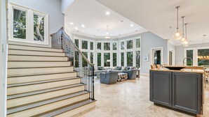 Amplia sala de estar con un gran ventanal, una escalera y una isla de cocina.