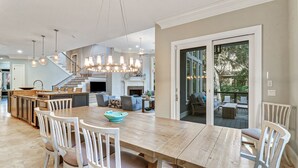 Un comedor espacioso con una mesa de madera y sillas blancas, una cocina con electrodomésticos de acero inoxidable y una escalera que lleva a un nivel superior.