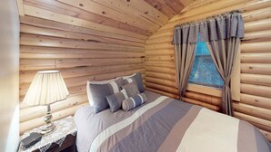A cozy log cabin bedroom with a bed, a lamp, and curtains. - The Cabin at Lydias Canyon (Glendale)