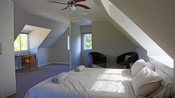 A bedroom with a bed, a desk, two chairs, and a ceiling fan.