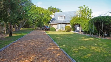 A house with a gravel driveway leading to a front door, surrounded by a well-maintained lawn and trees.