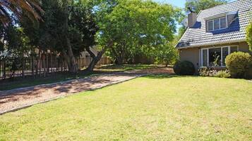 A house with a well-maintained lawn, a fenced yard, and a large tree.