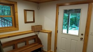 Eine hölzerne Bank mit einem Korb, eine weiße Tür mit Blick auf einen Wald und ein Spiegel an der Wand.