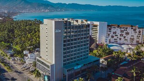 Un hotel de diseño moderno, con un llamativo letrero 'mio', rodeado de palmeras y vistas al océano.