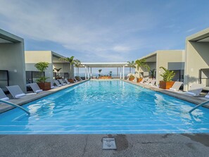 Una piscina con sillas de descanso y plantas en macetas, rodeada de edificios modernos.