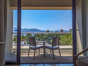 Un balcón con dos sillas de mimbre y una mesita, con vistas a un paisaje montañoso y palmeras.