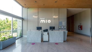 Zona de recepción de hotel con diseño moderno, que incluye un mostrador de recepción, computadoras y un ventanal con vistas a zonas verdes.