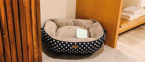 A pet bed with a polka dot design, a metal water bowl, and a wooden cabinet.