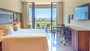 Habitación de hotel con cama, escritorio y grandes ventanales con vistas a la ciudad.