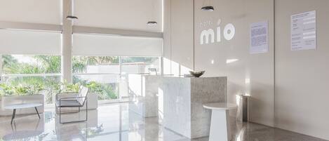 A modern hotel lobby with a reception desk, seating area, and large windows offering a view of greenery outside.