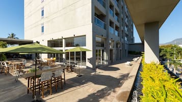 An outdoor patio area with tables and chairs, a water feature, and a view of a modern building with large windows.