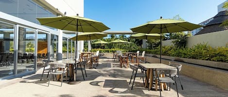 An outdoor patio area with tables and chairs, green umbrellas, and a glass building in the background.