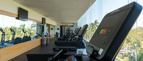 A gym with treadmills, exercise bikes, and a large window overlooking palm trees.