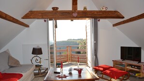 A cozy loft bedroom with a large window, wooden beams, a bed, a small table with candles, and a TV. - Chaletde montagne indépendant en Alsace Massif du Champ du Feu - Ski resort  (Bellefosse)