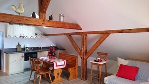 A cozy loft-style room with exposed wooden beams, a kitchenette, a dining area with a wooden table and chairs, and a bed with a red pillow. - Chaletde montagne indépendant en Alsace Massif du Champ du Feu - Ski resort  (Bellefosse)