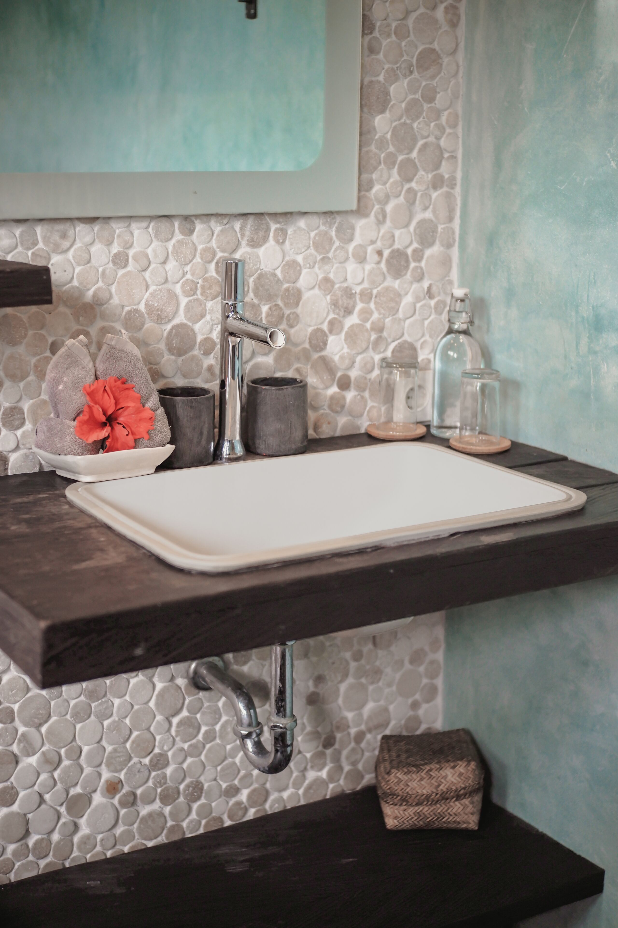 A bathroom with a stone mosaic backsplash, a white sink, dark countertops, and a mirror above the sink.