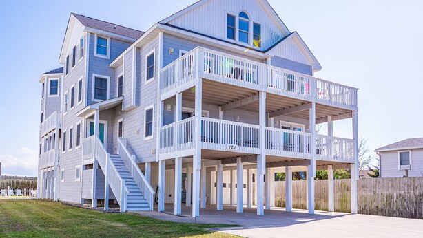 Une maison à plusieurs étages située en bord de mer, dotée d’un balcon, d’un escalier et d’une plaque portant le numéro « 121 ».