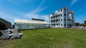 Un bâtiment moderne doté d’une véranda en verre, d’une pelouse verdoyante et d’un espace extérieur aménagé pour s’asseoir.