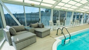 Un espace piscine intérieure doté d'un toit en verre, de fauteuils de relaxation en osier et d'un escalier pour accéder à la piscine.