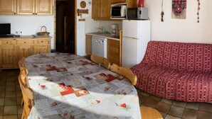 Une pièce chaleureuse avec un plafond en bois, une table à manger recouverte d’une courtepointe, un canapé et un coin cuisine équipé d’un four à micro-ondes et d’un réfrigérateur.