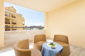 Un balcon avec des fauteuils en osier et une table, d’où l’on peut admirer un immeuble doté de balcons et un ciel dégagé.