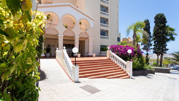 A hotel entrance with a staircase leading to the main building, surrounded by greenery and a clear sky. - Apartment in Castle Harbor, heated pool, satellite TV channels (Los Cristianos)
