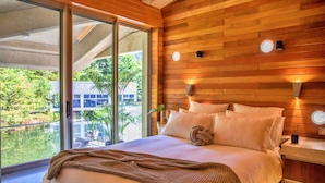Ein modernes Hotelzimmer mit einem großen Bett, Holzpaneelen und einer Glasschiebetür, die auf einen Balkon mit Blick auf Grünflächen führt.
