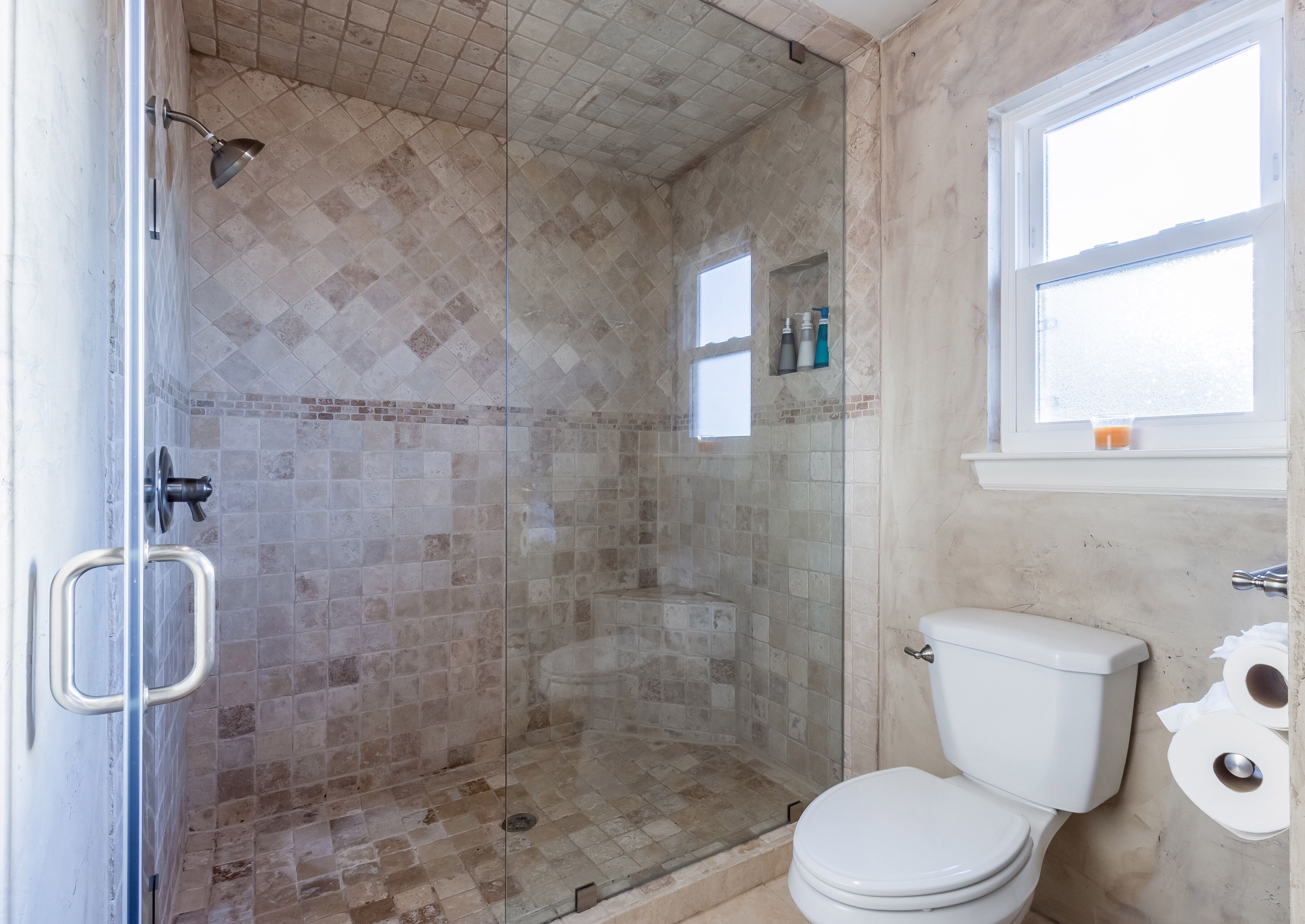 A bathroom with a glass-enclosed shower, a toilet, and a window.