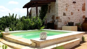 Ein Pool mit einer Steindeck, umgeben von Grünpflanzen und einem Steinhaus mit einer Pergola.