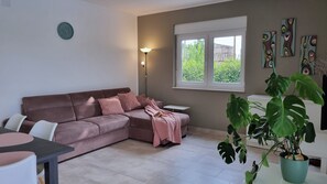 Una sala de estar con un sofá marrón, una mesita, una lámpara y una ventana que da a zonas verdes.