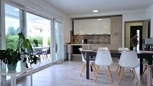A modern kitchen with white cabinets, a tiled backsplash, and a dining area with white chairs and a black table. - Aria, villa in Filipana, close to numerous beaches and activities (Marcana)