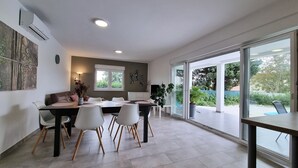 A modern dining area with a large table, white chairs, and a brown sofa. There is a large window providing a view of the outdoors. - Aria, villa in Filipana, close to numerous beaches and activities (Marcana)