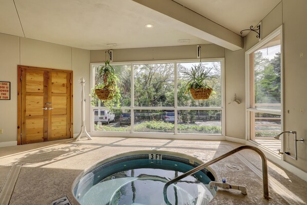 A spa room with a hot tub, large windows, and a view of the outside.