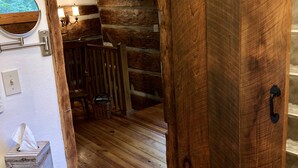A rustic wooden interior with a wooden door, a small white table with a tissue box, and a wooden bench. - Quaint, Romantic Mountain Antique Log Cabin near Asheville! (Fairview)