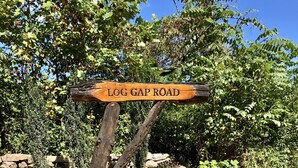 A wooden sign reading "LOG GAP ROAD" with a stone wall and potted plants in the foreground. - Quaint, Romantic Mountain Antique Log Cabin near Asheville! (Fairview)