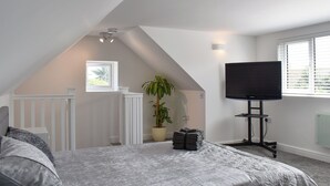 Un dormitorio con techo inclinado, una cama, un televisor, una ventana y una planta.