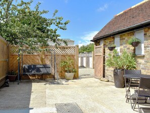 Un jardin avec une clôture en bois, un téléviseur, du mobilier d’extérieur et des plantes en pot.