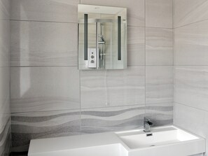 Une salle de bain moderne avec une douche à parois de verre, un lavabo blanc et un mur recouvert de carreaux formant un motif ondulé.