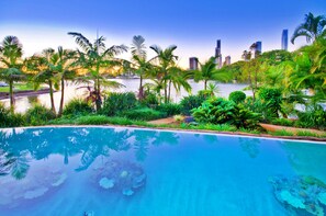 Una piscina con agua cristalina que refleja palmeras y el horizonte de la ciudad al fondo.