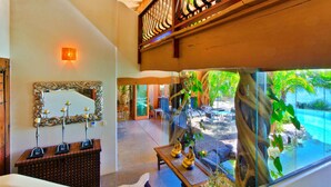 A spacious indoor area with a large window overlooking a pool and lush greenery. There is a decorative mirror on the wall and a wooden bench with small statues. - Casa Albero Via Roma (Surfers Paradise)