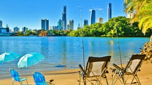 A beach with chairs and umbrellas, a city skyline in the background, and a calm body of water. - Casa Albero Via Roma (Surfers Paradise)