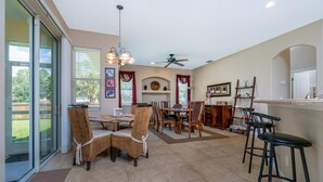 A spacious kitchen with a dining area, featuring a large island, bar stools, and a ceiling fan.