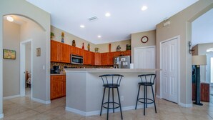 A kitchen with wooden cabinets, a central island with bar stools, a microwave, and a refrigerator.