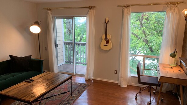 Ein geräumiges Wohnzimmer mit einem grünen Sofa, einem Holztisch, einer Gitarre und einem Schreibtisch mit einer Lampe.