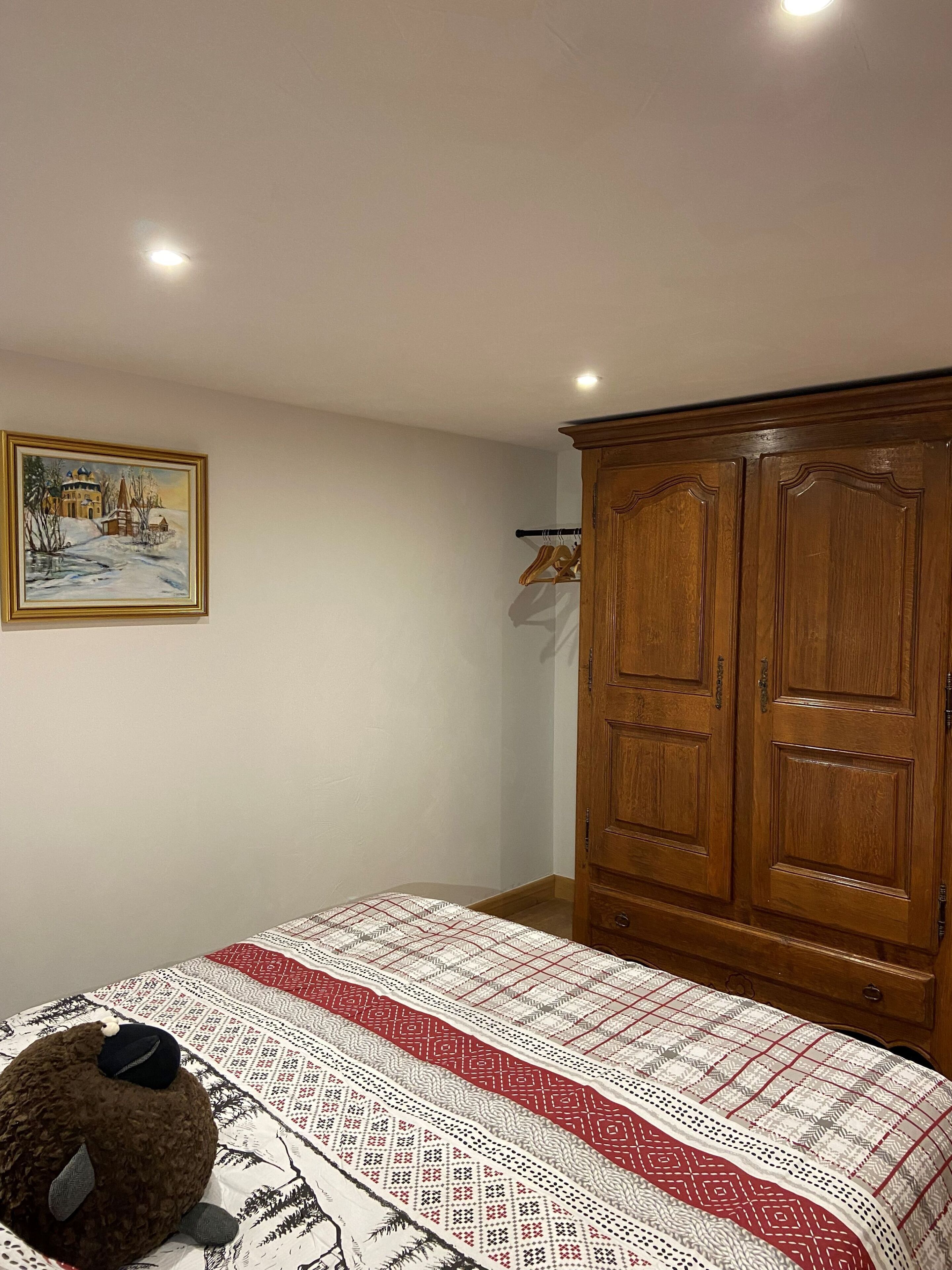Un dormitorio con cama, un armario de madera, un cuadro en la pared y un perchero.