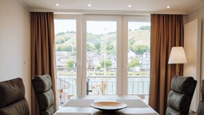 Una habitación de hotel moderna con un ventanal grande que da a un paisaje pintoresco, una mesa de comedor de madera con individuales y dos sillones de cuero.