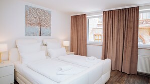 Una habitación de hotel con una cama grande, dos mesitas de noche, un ventanal con cortinas y un cuadro en la pared.