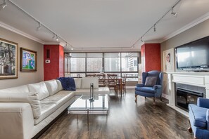 Relax in a stylish living room with a sofa, coffee table, and armchair, offering a city view and a fireplace with a mounted TV.