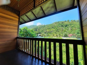 A wooden balcony with a view of a lush green landscape and a small building. - Hotel Besar Bulan Baru - Senggigi (Senggigi)